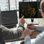 Closeup of two men data science specialists working at office together, analyzing big data on screen. Coders working on new project